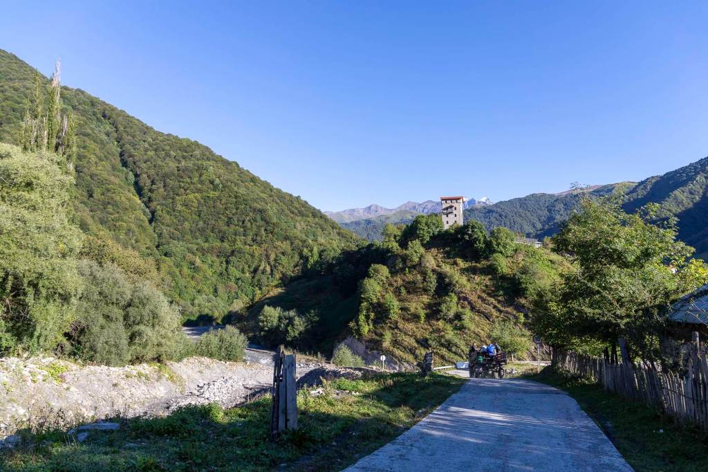 Een schilderachtig uitzicht op een berglandschap met weelderige groene heuvels en een toren op een heuveltop, onder een heldere blauwe lucht.