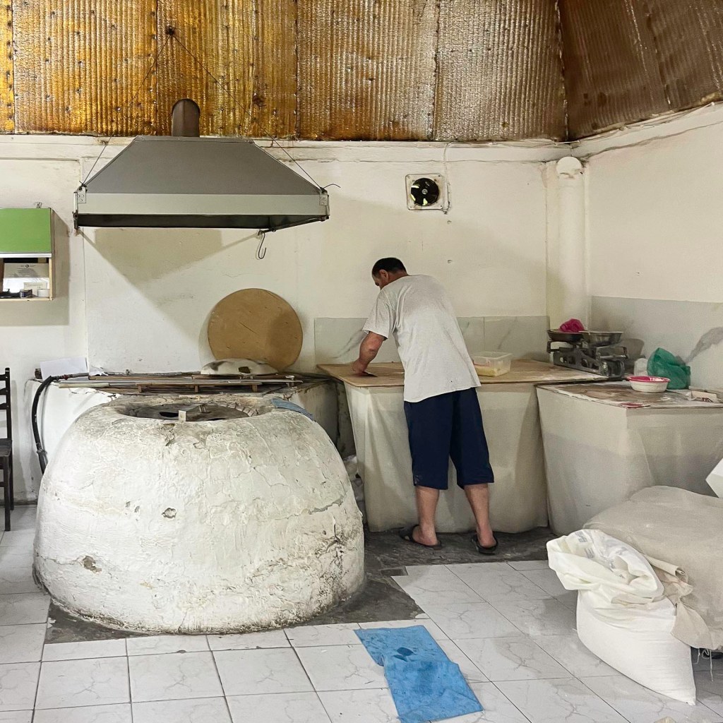 Een man bezig met het voorbereiden van deeg in een traditionele bakkerij met een ronde oven.