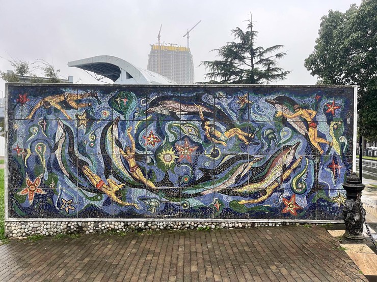 Mosaic muurschildering met een onderwaterlandschap, inclusief verschillende vissen, zeesterren en andere zeedieren, op een grijze en bewolkte dag.